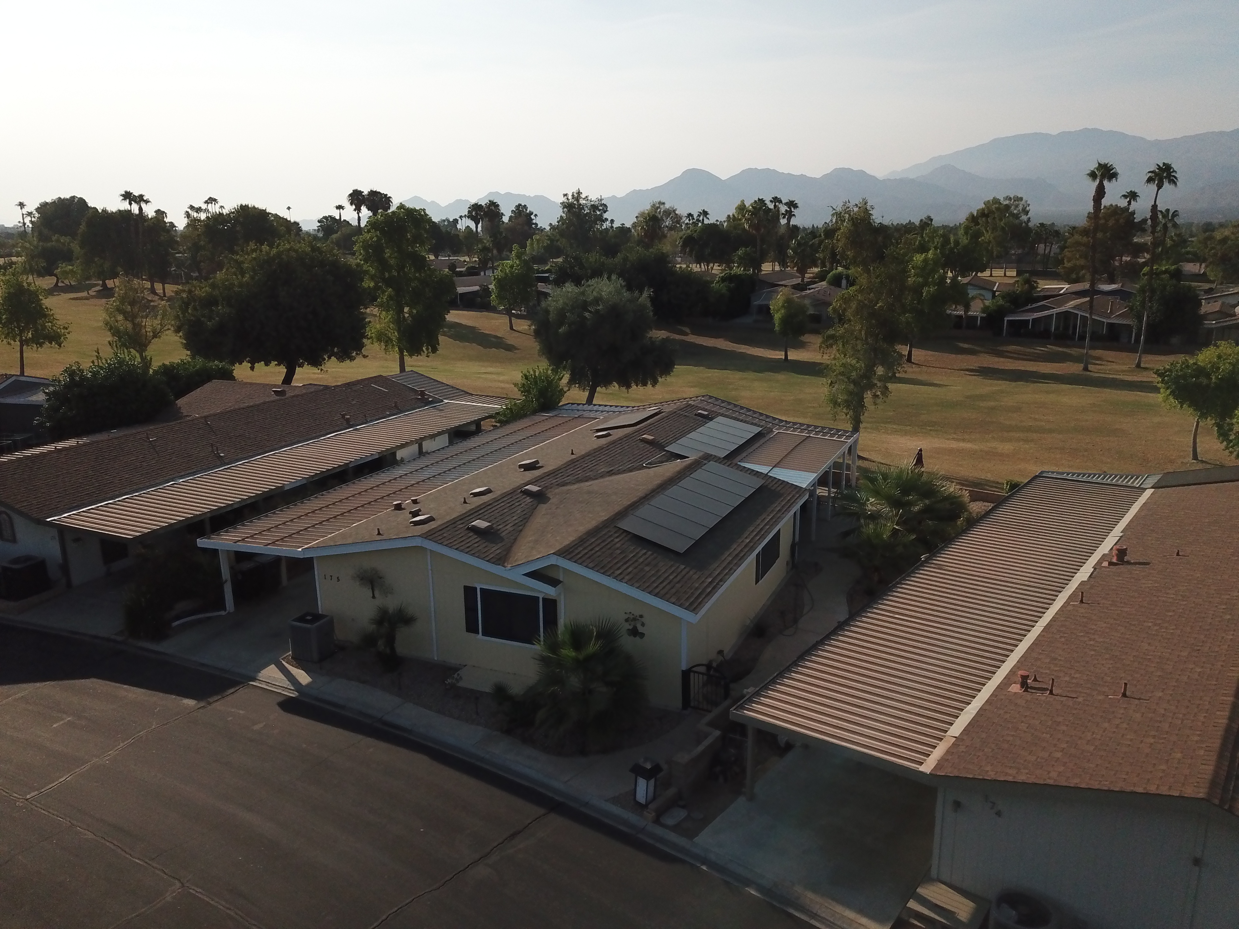 Solar panel installation on a manufactured home in a residential area with palm trees and mountains in the background, showcasing energy-efficient solutions for mobile homeowners in Southern California.